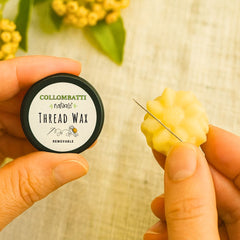 A person holding a container of Collombatti Beeswax Thread Wax with a piece of wax and a needle.