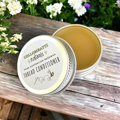 Collombatti Naturals Pure Australian Beeswax Thread Conditioner in a reusable tin. The smooth, solid beeswax sits inside the tin, ready for conditioning sewing and embroidery threads. Photographed on a rustic wooden surface with fresh flowers in the background, this natural thread wax is perfect for reducing tangles, strengthening fibres, and enhancing stitching ease.