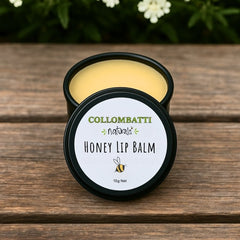 Collombatti Naturals Honey Lip Balm in a round, reusable tin, placed on a rustic wooden surface with delicate white flowers in the background. The smooth, golden balm is made with Australian beeswax, honey, and nourishing natural ingredients to hydrate and protect lips. The tin features a minimalist label with a bee illustration, reflecting the brand’s eco-friendly and handcrafted approach.