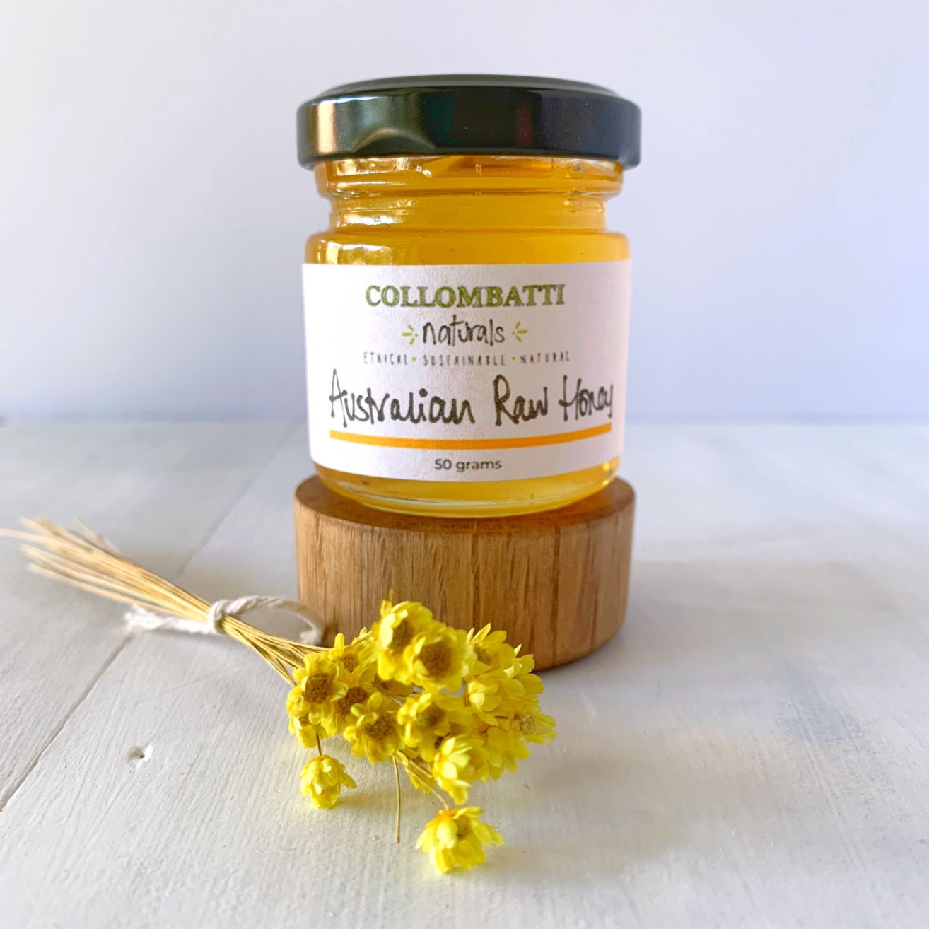 Collombatti Naturals sample size honey sitting on a block of wood with yellow flowers